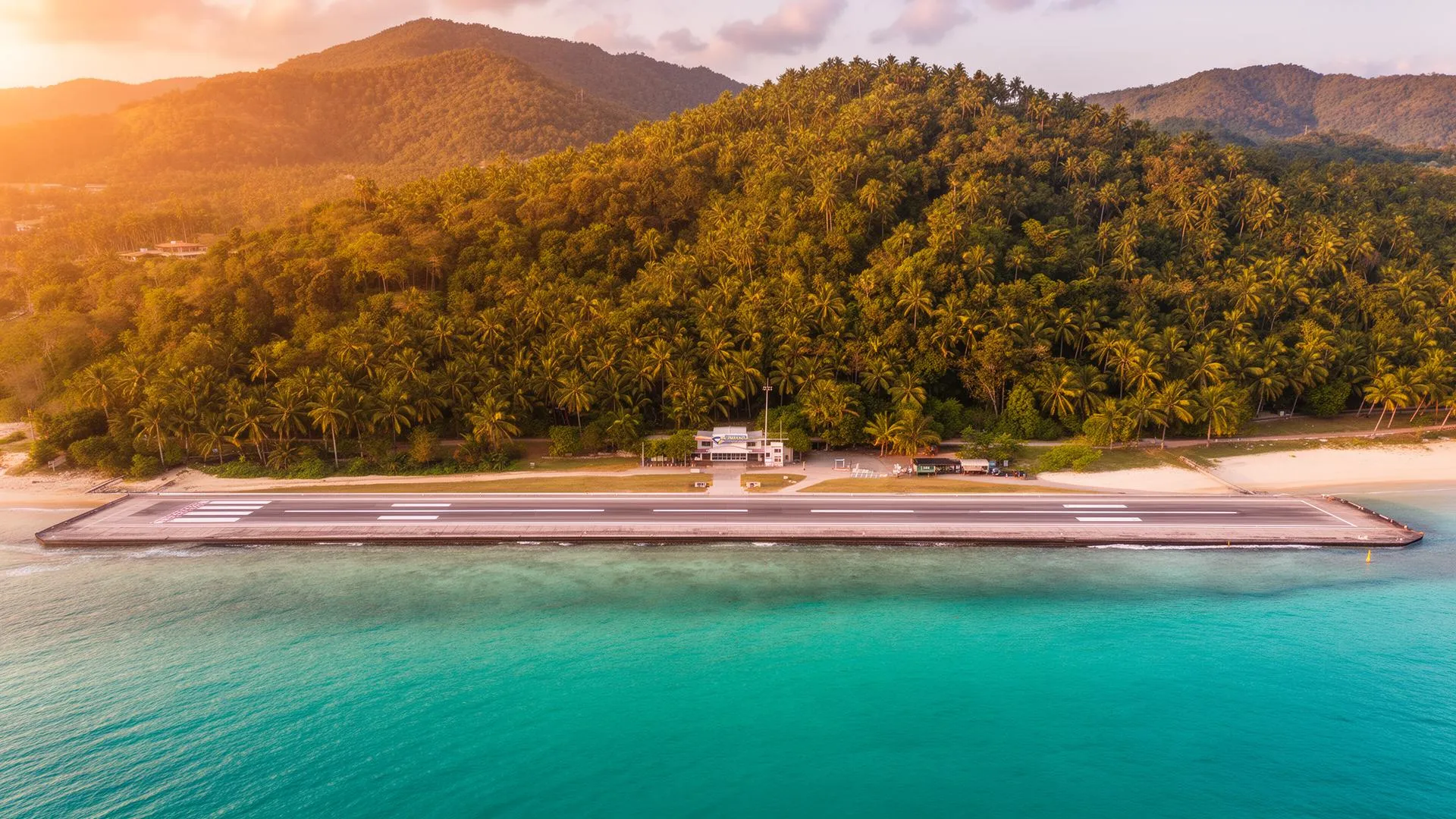 Aerial view of Koh Samui Airport runway surrounded by tropical hills and turquoise Gulf of Thailand water at golden hour